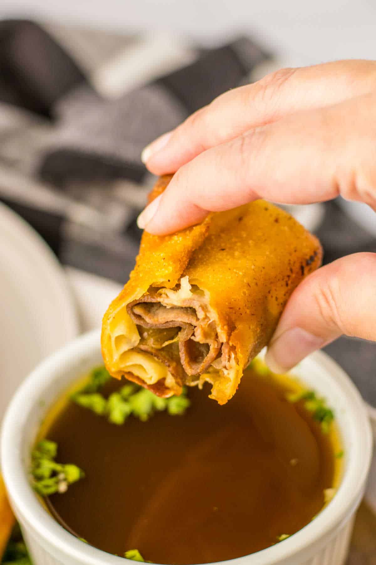 A hand holding a French dip egg roll cut in half over dipping sauce.