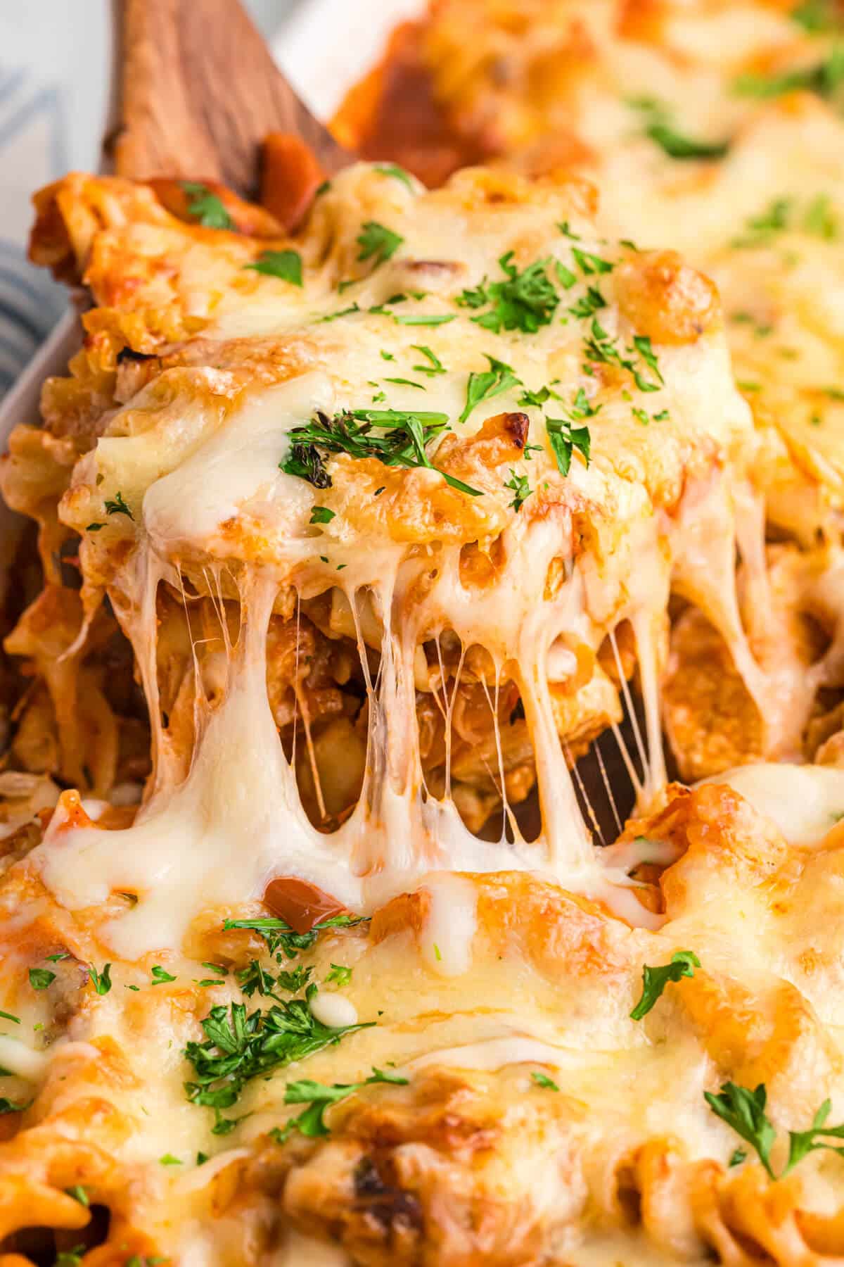 A wooden spatula lifting out baked chicken and tarragon pasta from a casserole dish.