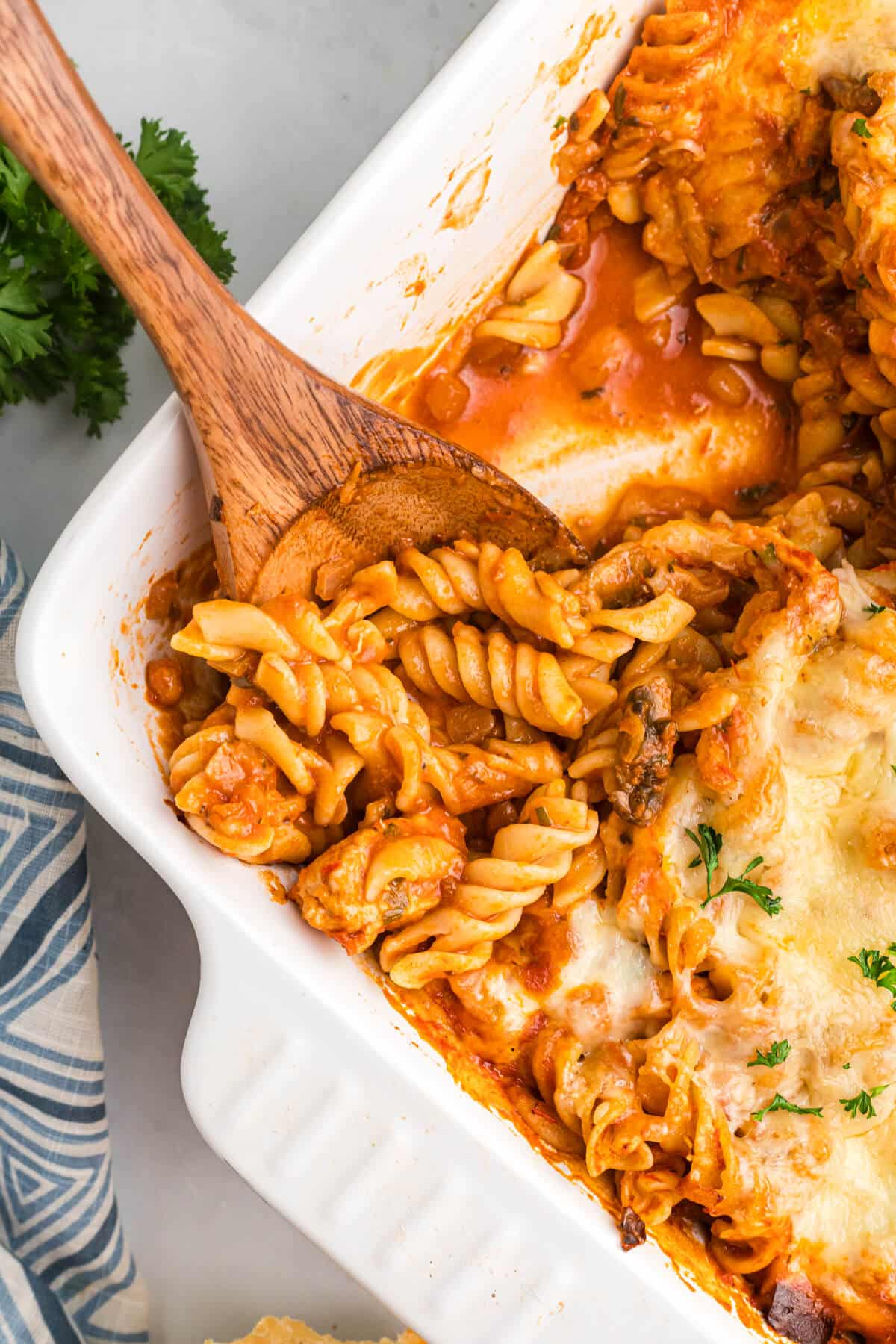 A wooden spoon in a pan of baked chicken and tarragon pasta.