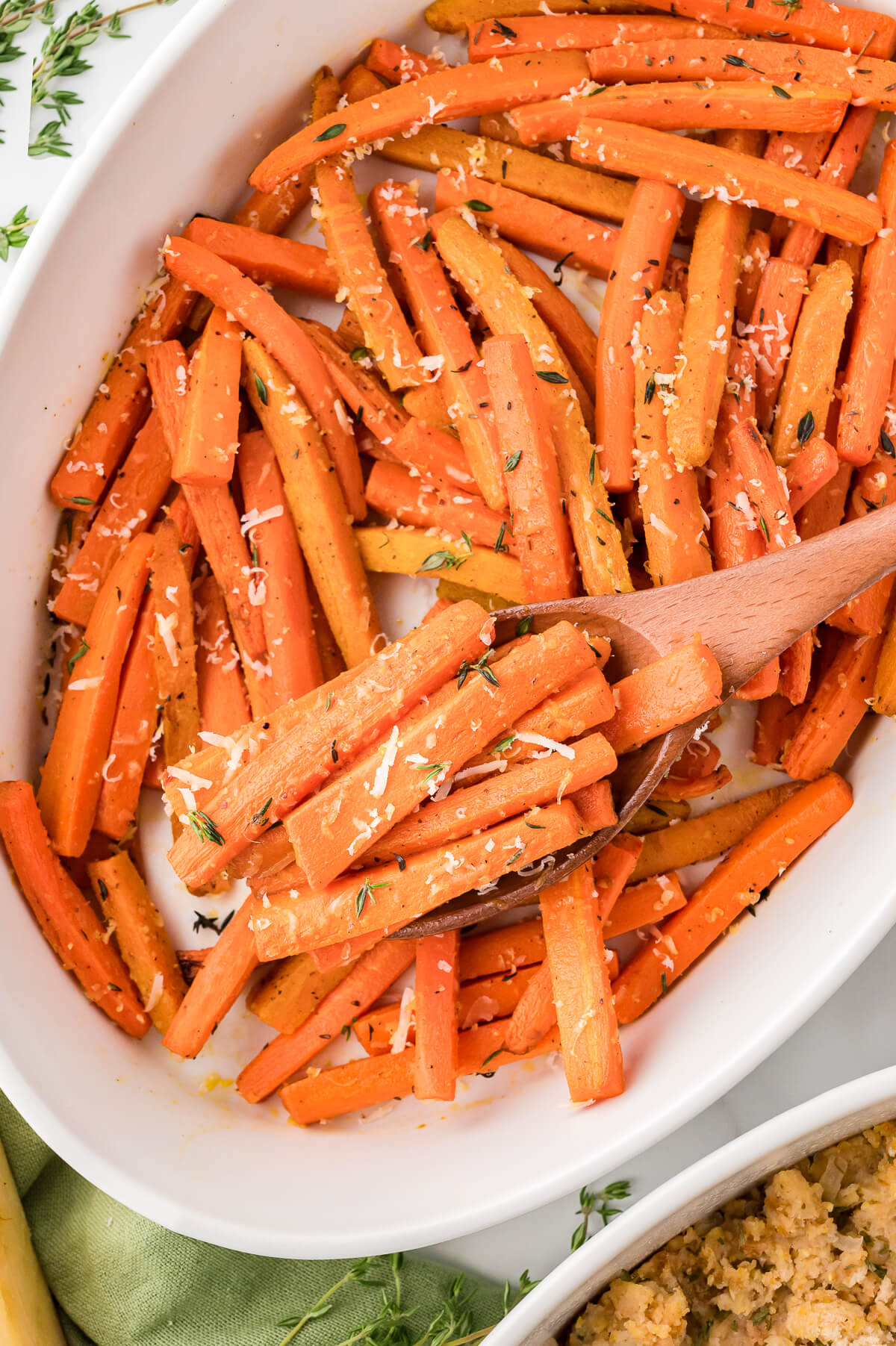 Parmesan roasted carrots in a casserole dish with a wooden spoon.