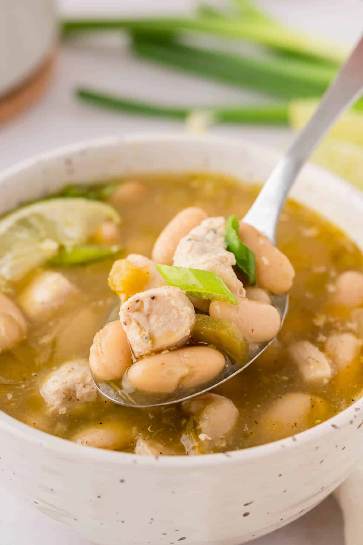 A bowl of salsa verde chicken soup with a spoon in it.