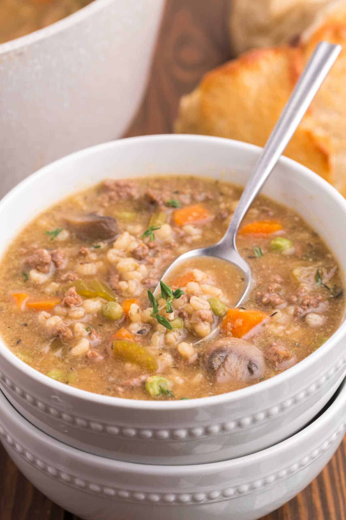 A bowl of beef and barley soup with a spoon.