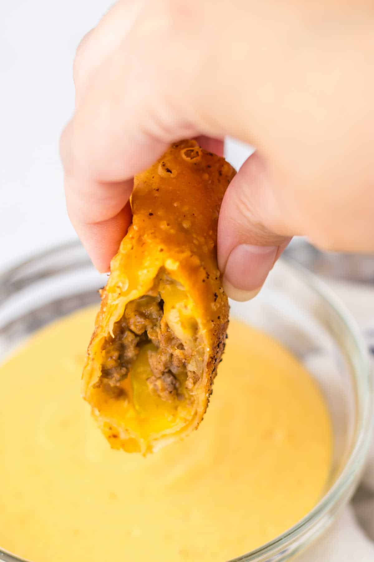 A hand holding a cut Big Mac egg roll over dipping sauce.