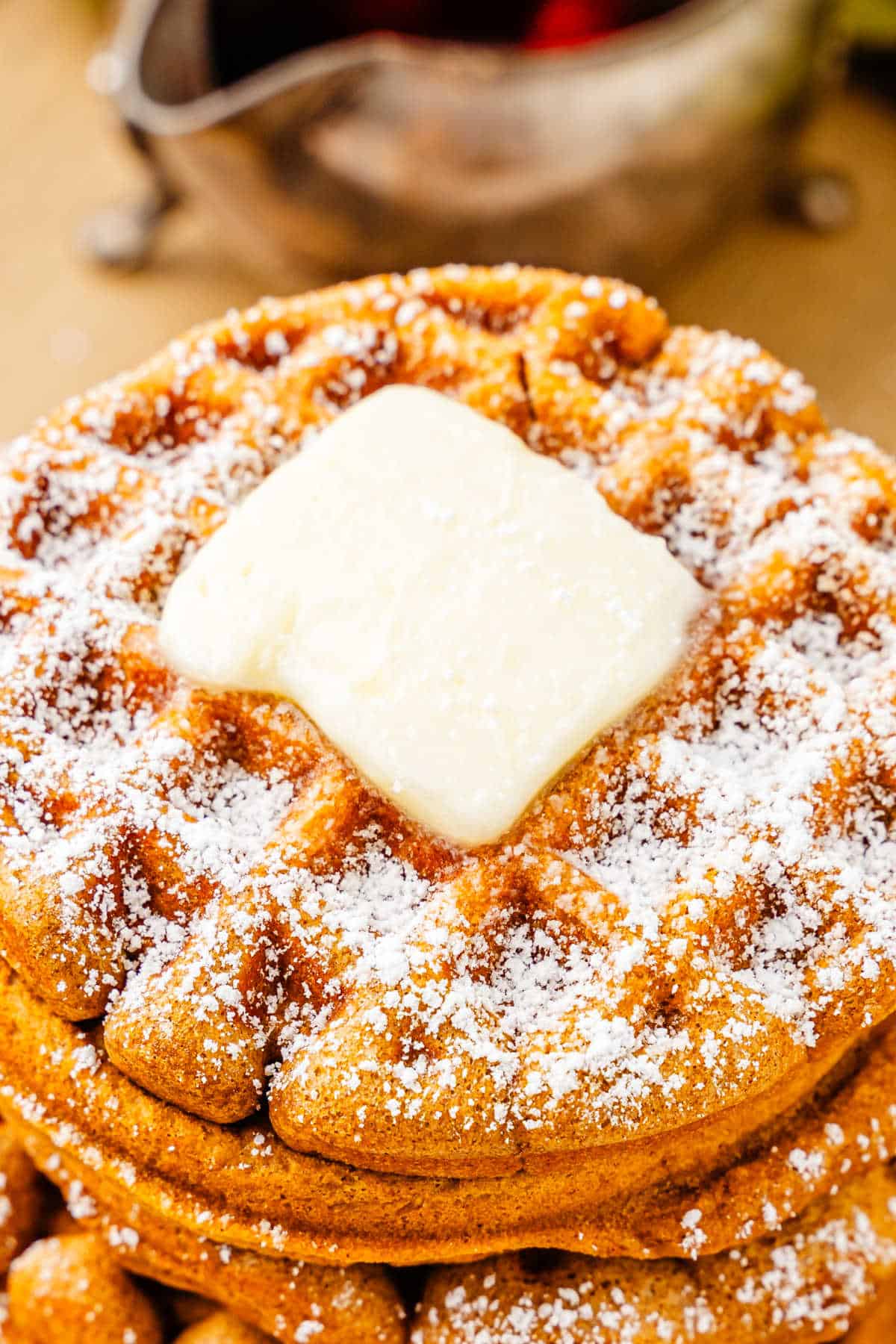 A plate of gingerbread waffles with butter and powdered sugar on top.