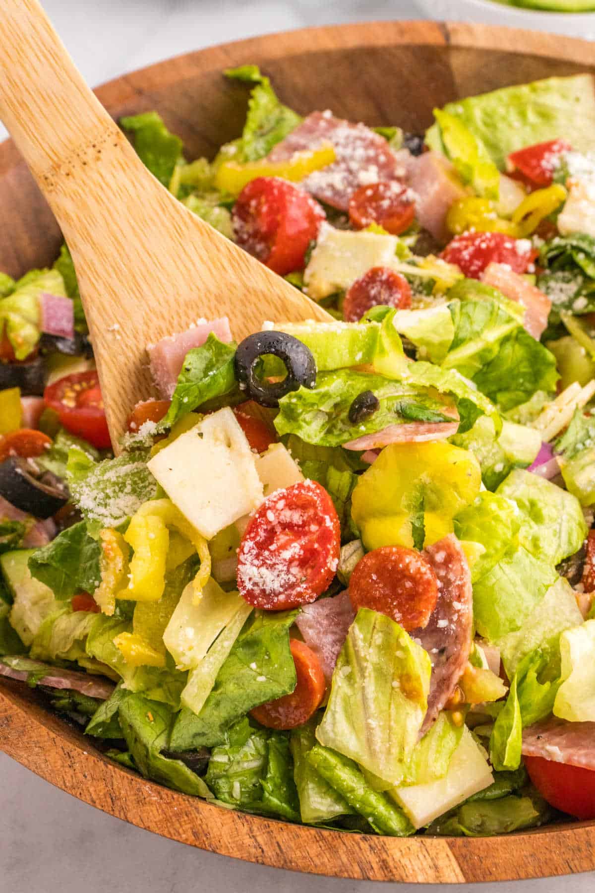 Italian sub salad in a bowl with a wooden spoon.