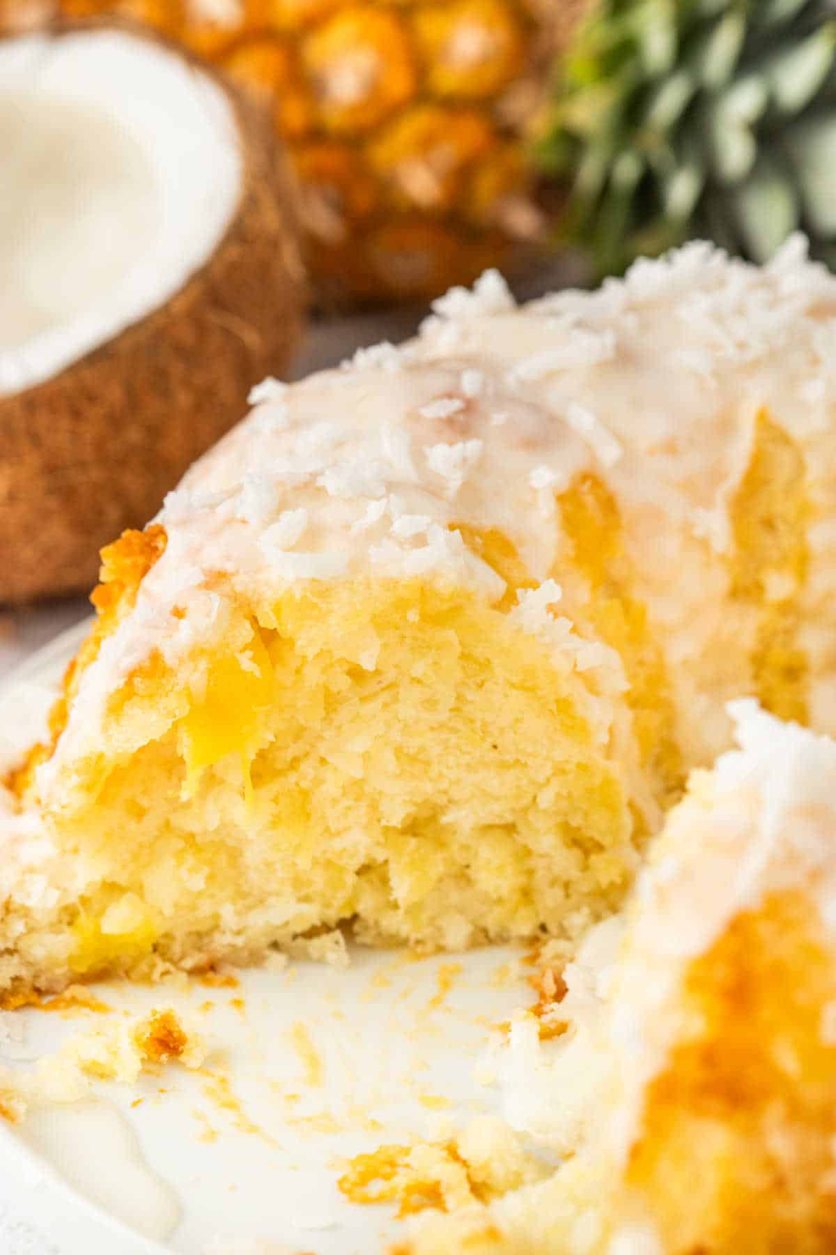 A pineapple coconut bundt cake on a platter with a piece missing.