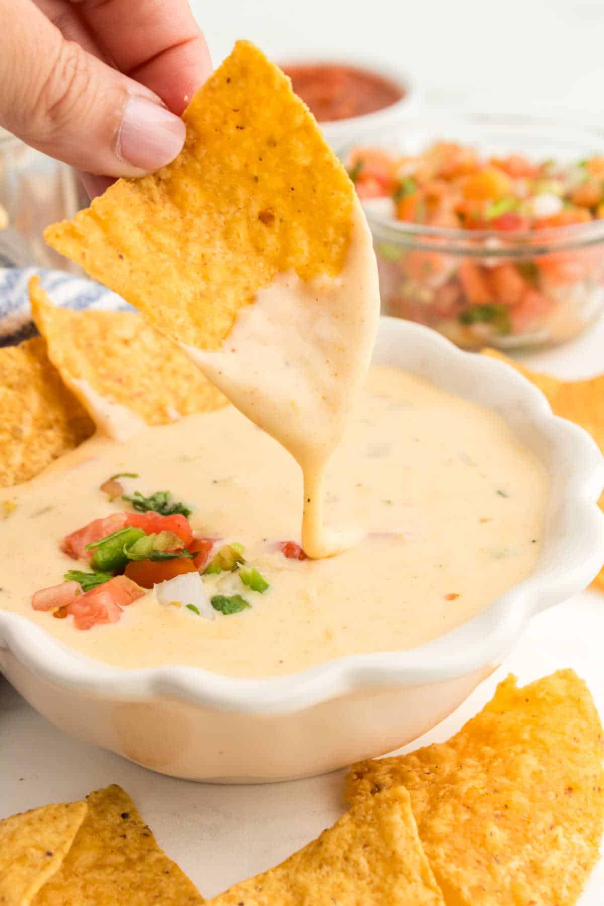A hand dipping a tortilla chip in queso.