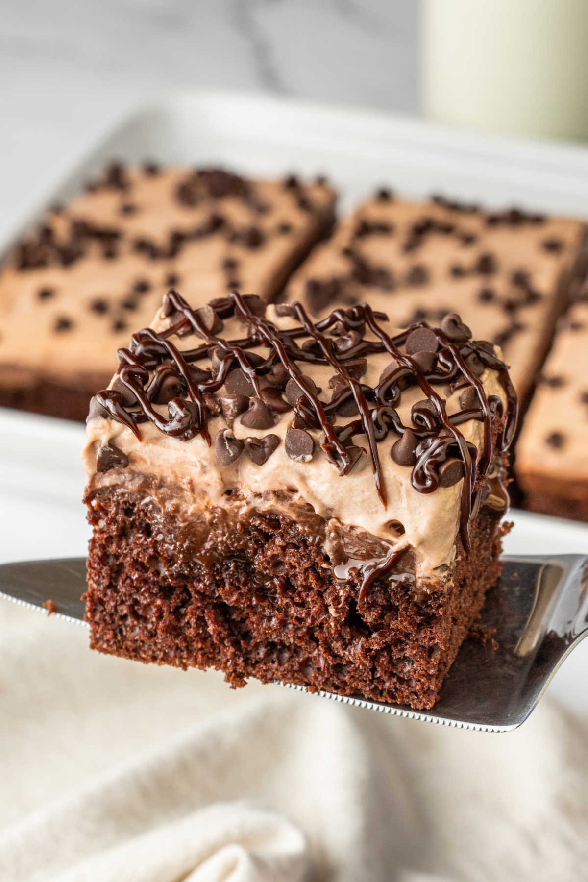 A piece of triple chocolate poke cake on a serving spatula.