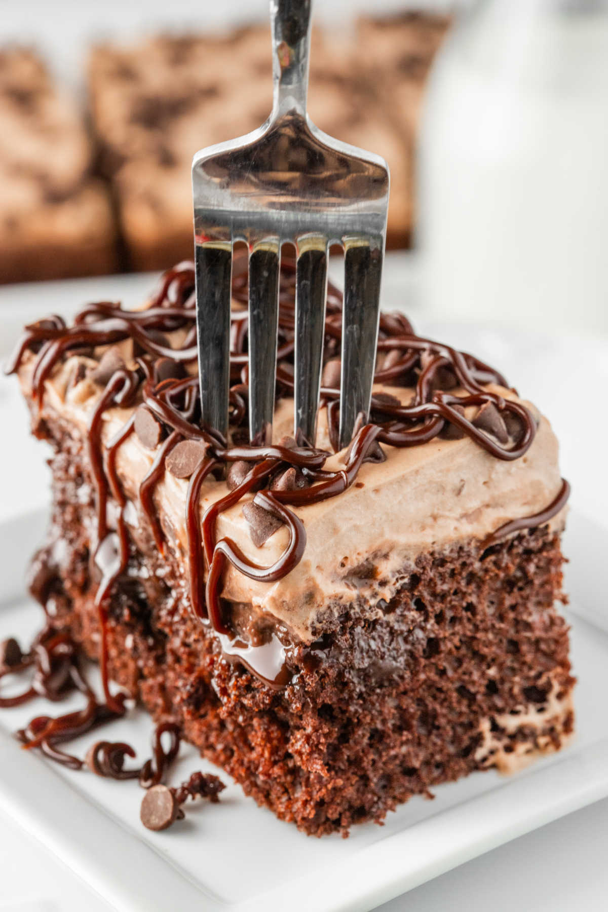 A piece of triple chocolate poke cake on a plate with a fork in it.