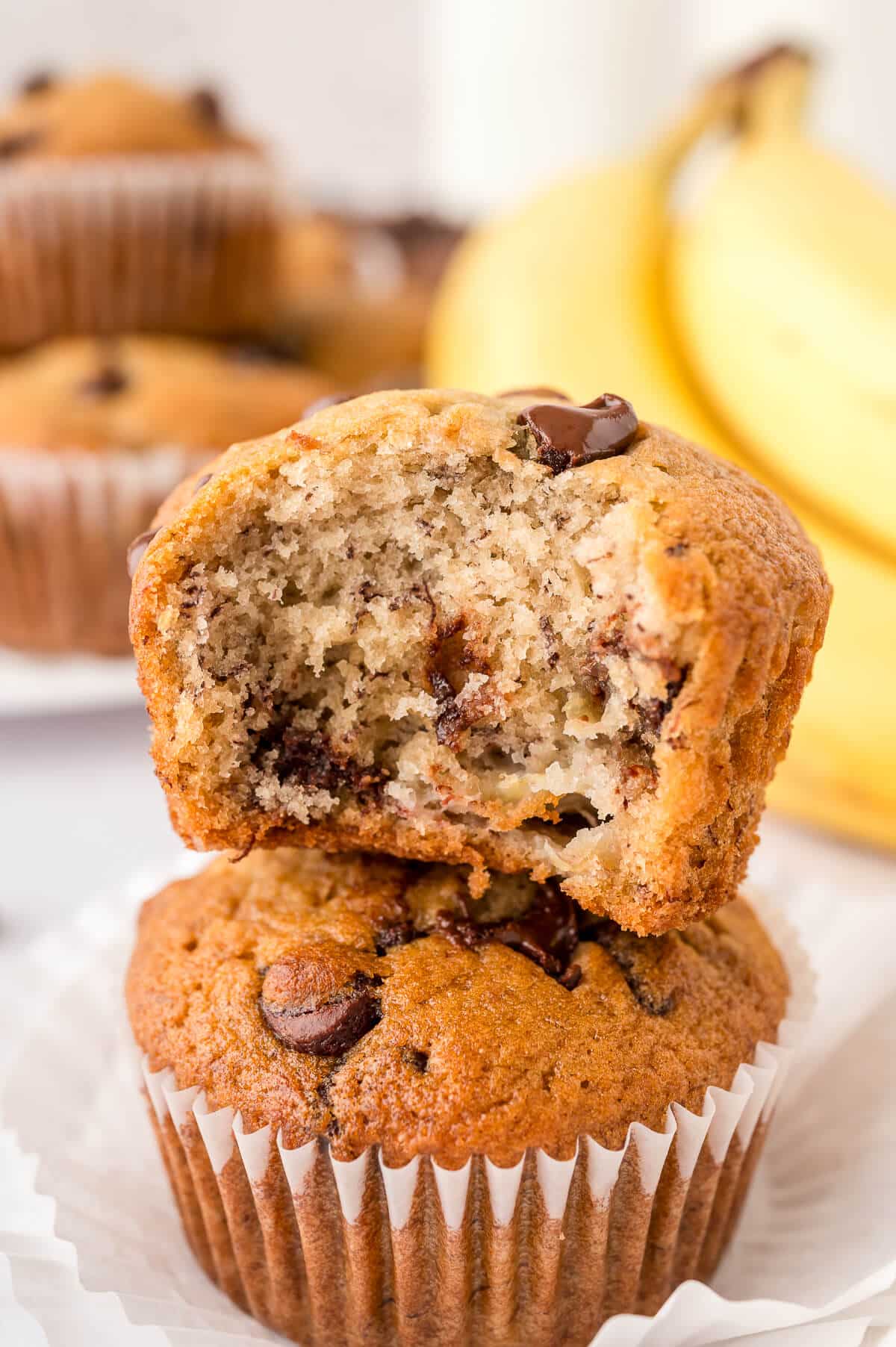 A stack of banana chocolate chip muffins with a bite out of the top muffin.