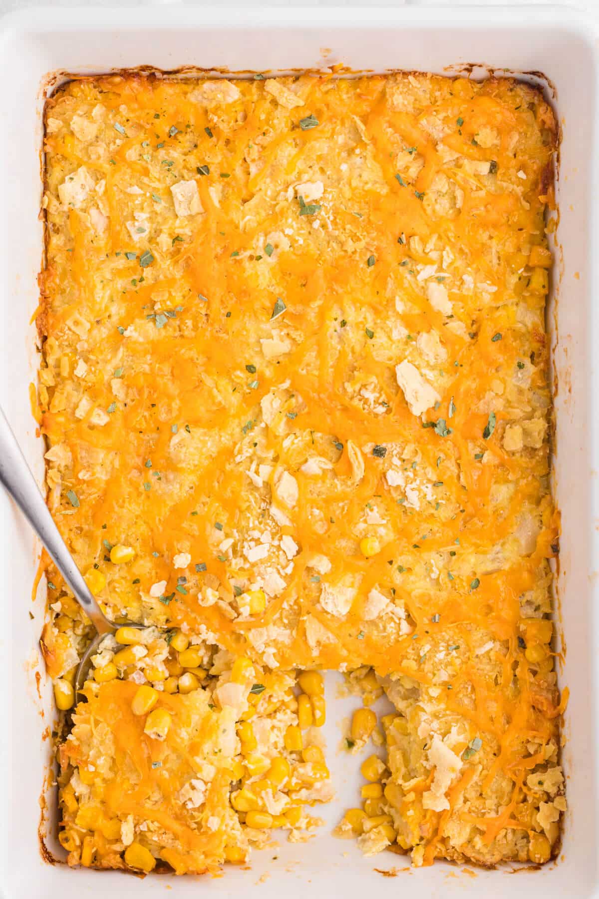 Cheesy corn casserole in a pan with a serving spoon.
