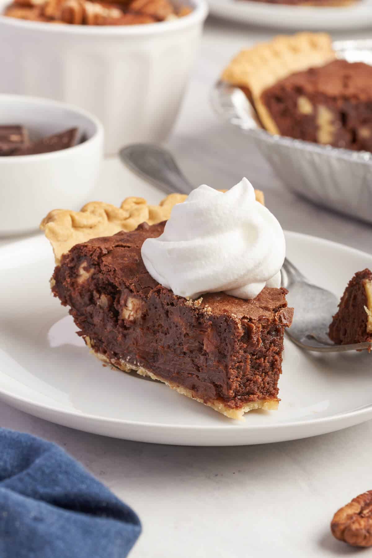 A slice of chocolate pecan pie on a plate with a bite off the end.