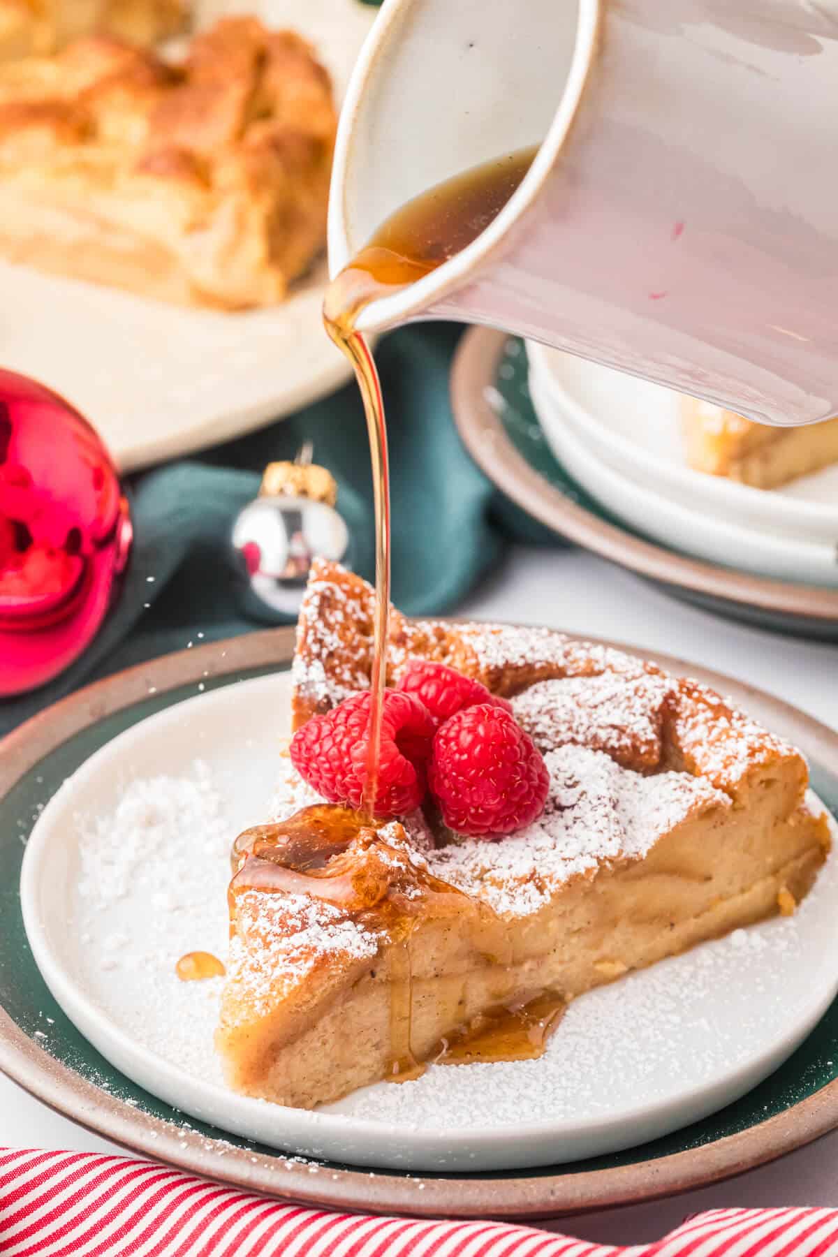 A slice of eggnog bread pudding on a plate with syrup being poured on it.