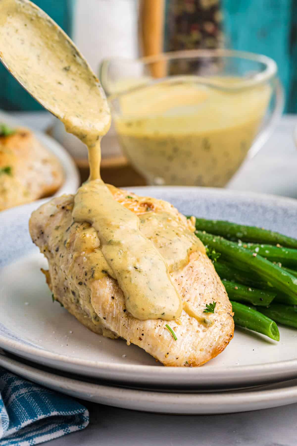 A spoon pouring mustard sauce on a chicken breast.