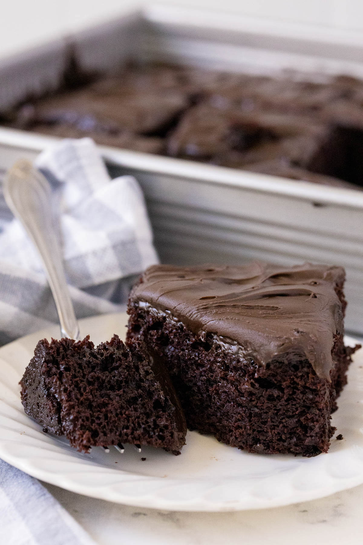 A piece of wacky cake on a plate with a piece on a fork.