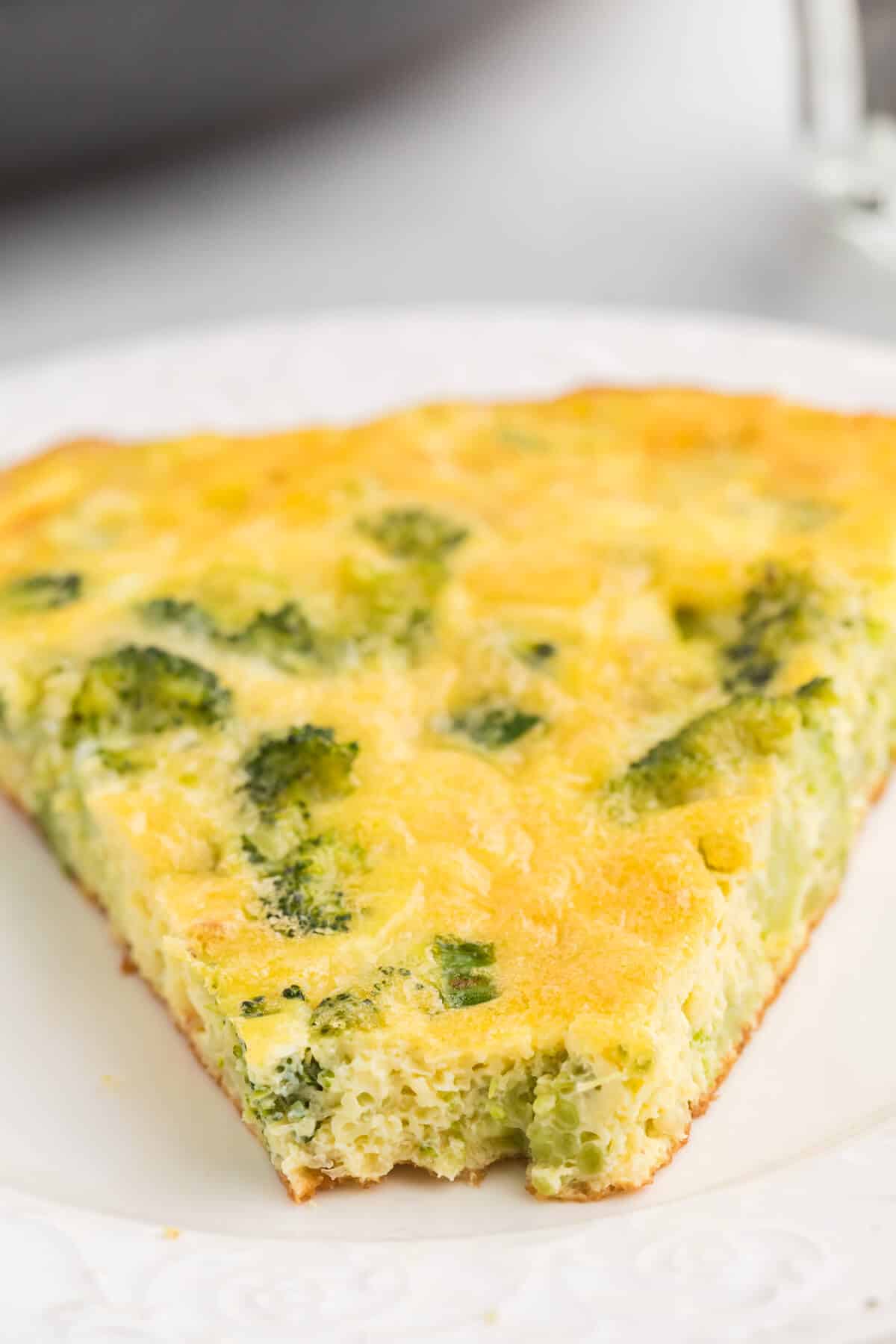 A slice of broccoli frittata on a plate with a bite off the end.