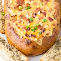 Cheesy bacon bread bowl on a wooden cutting board.