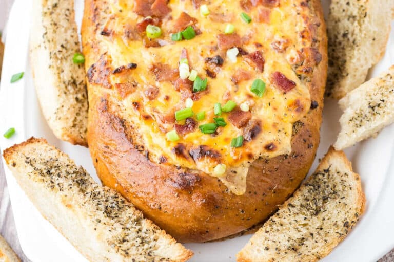 Cheesy bacon bread bowl on a wooden cutting board.