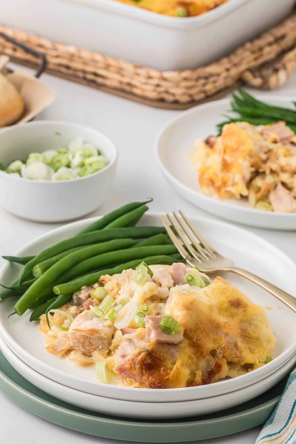 Chicken cordon bleu casserole on a plate with green beans and a fork.