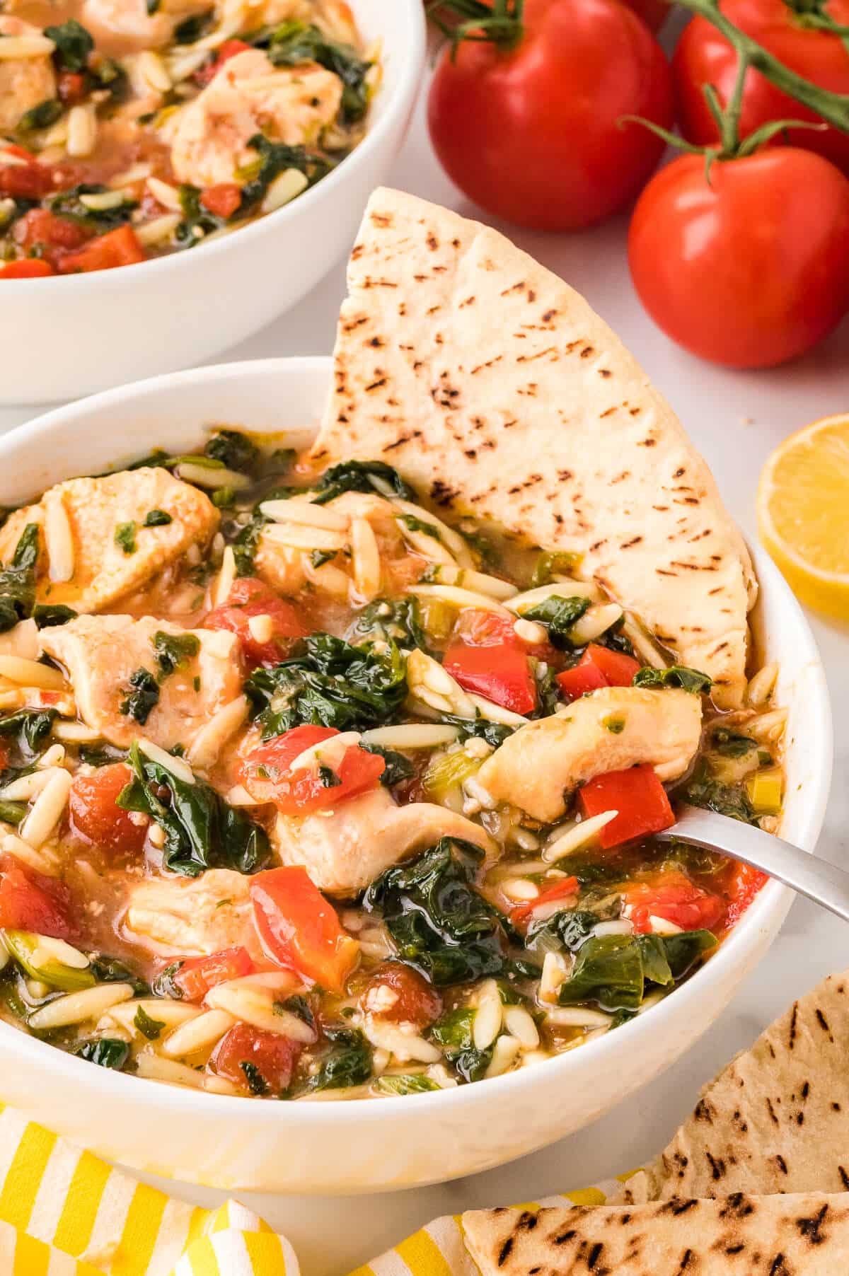 A bowl of Greek Chicken Orzo Soup with a pita in it.