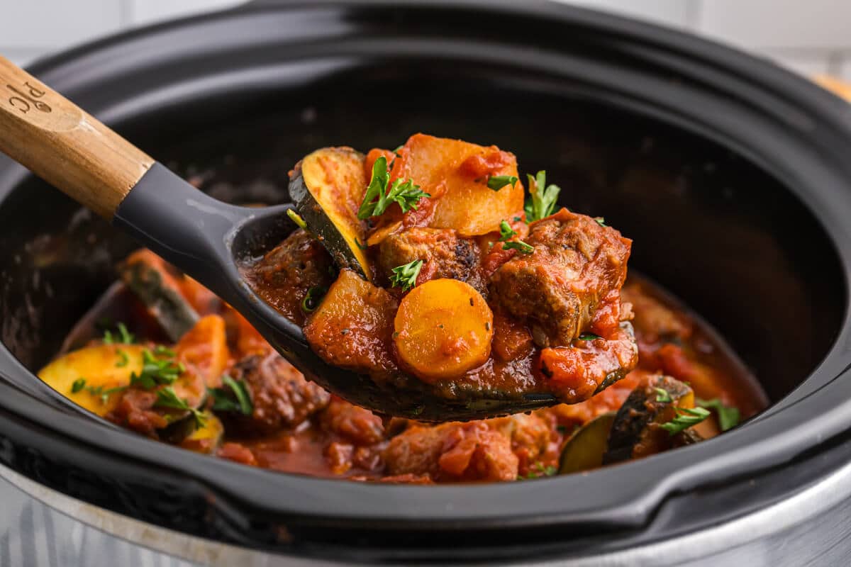 Italian sausage and vegetable stew on a serving spoon.