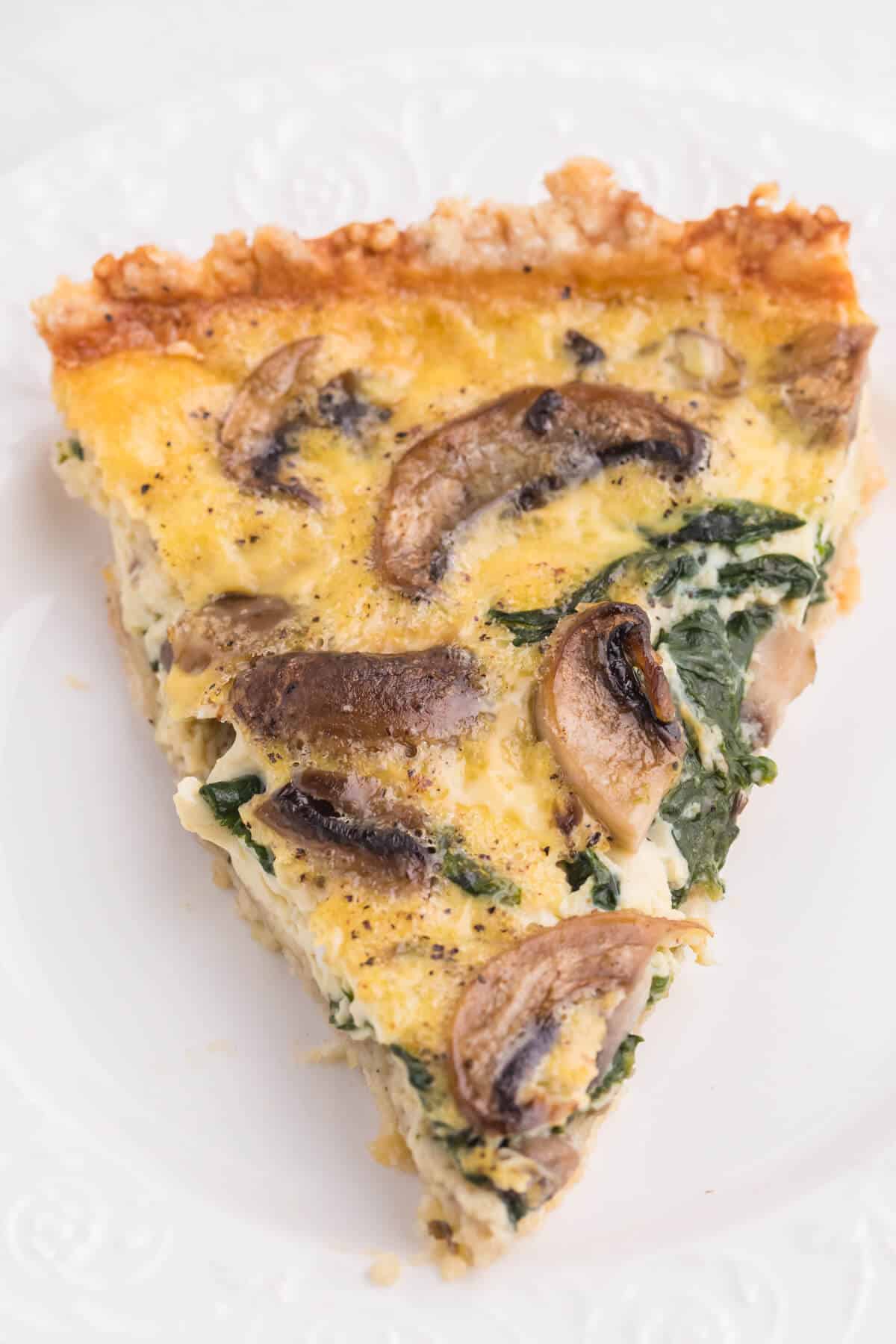 A slice of spinach mushroom quiche on a plate.