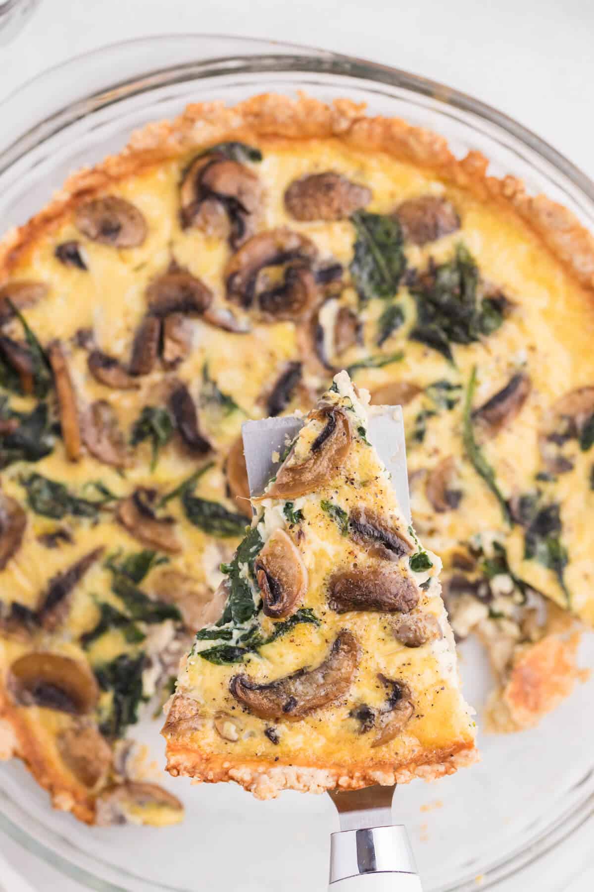 A slice of spinach mushroom quiche on a serving spatula.