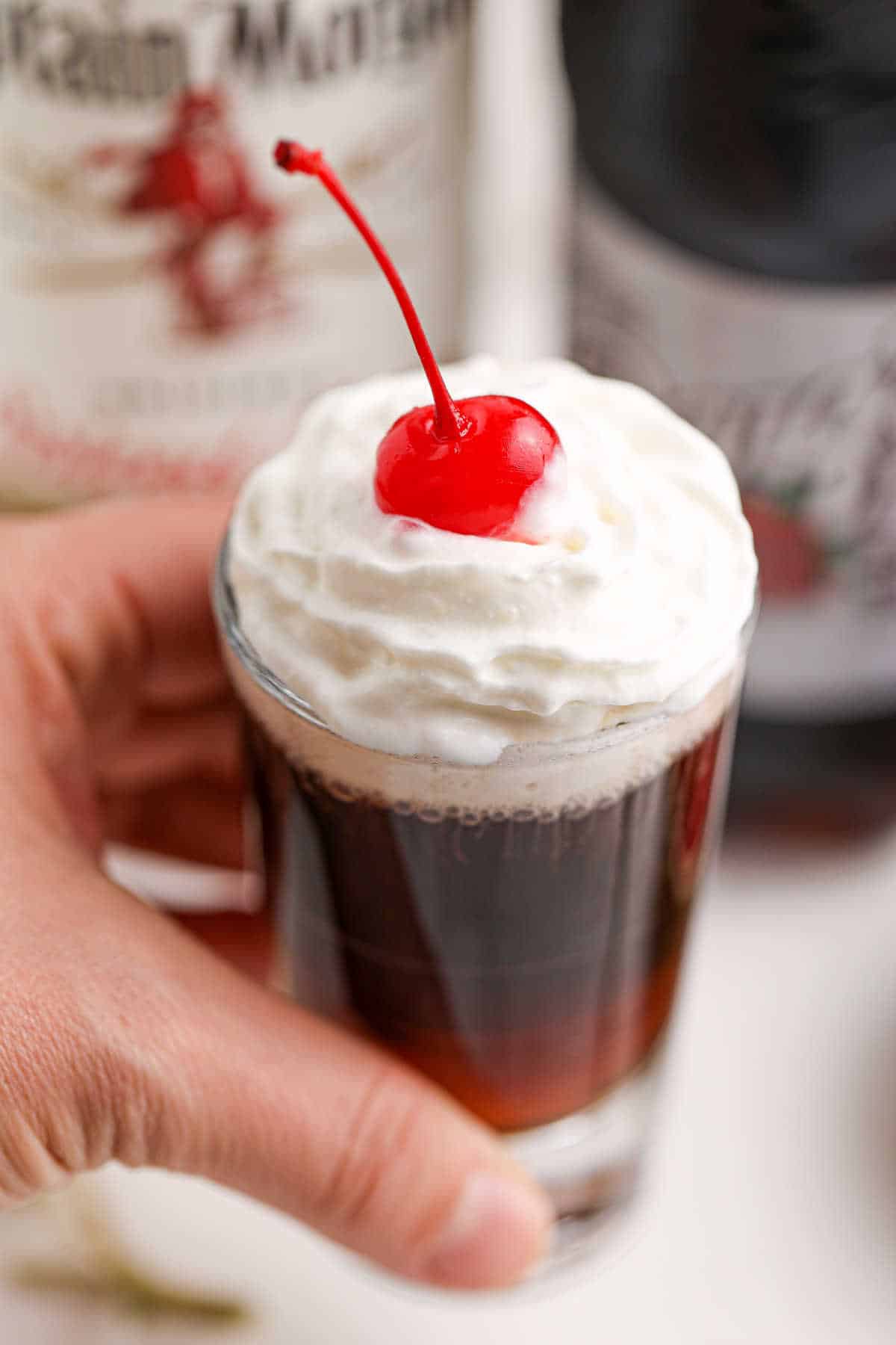 A hand holding a root beer shooter.