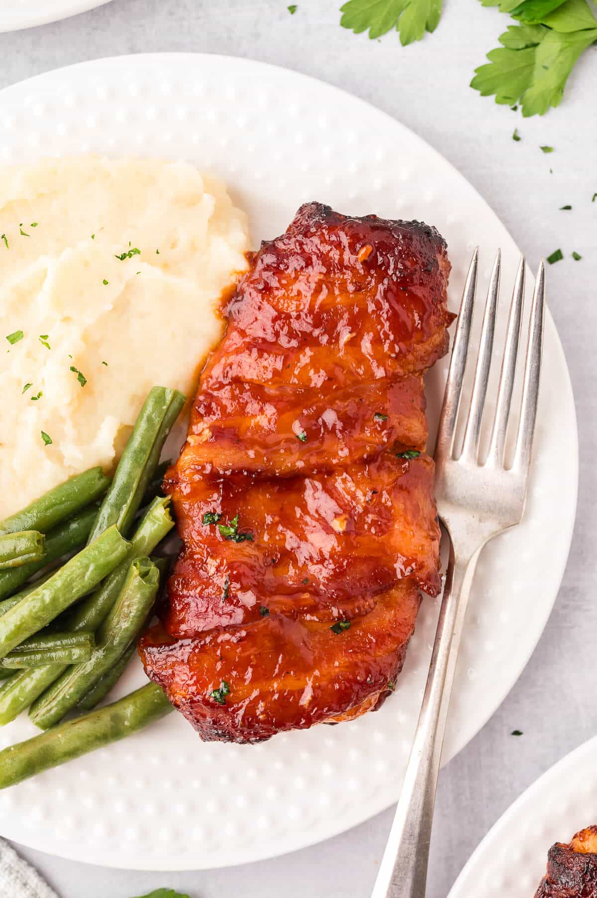 A bacon wrapped chicken on a plate with mashed potatoes and green beans.