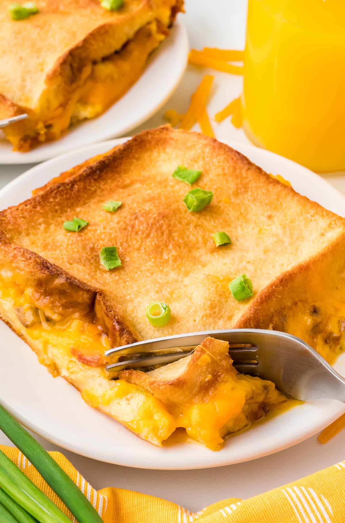 A piece of overnight bacon breakfast casserole on a plate with a fork.