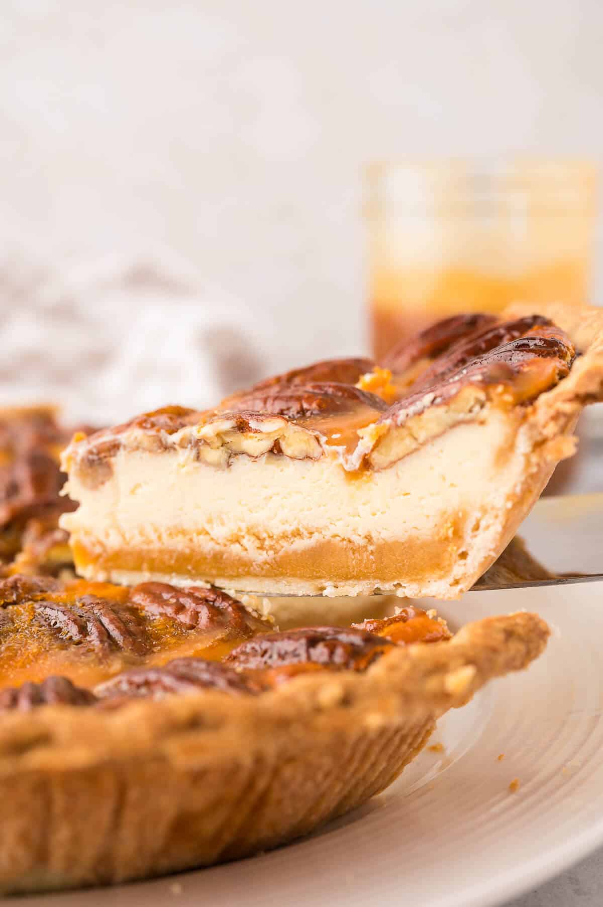 A slice of pecan pie cheesecake on a serving spatula.