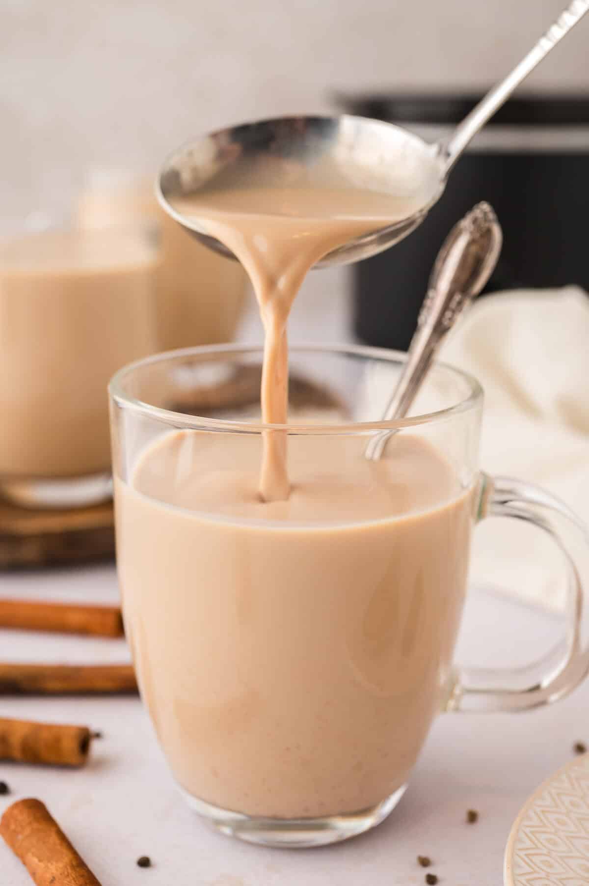 A ladle pouring chai latte into a glass mug.