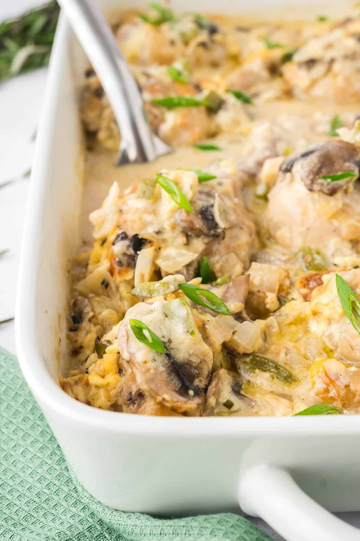 Smothered chicken in a baking pan with a serving spoon.