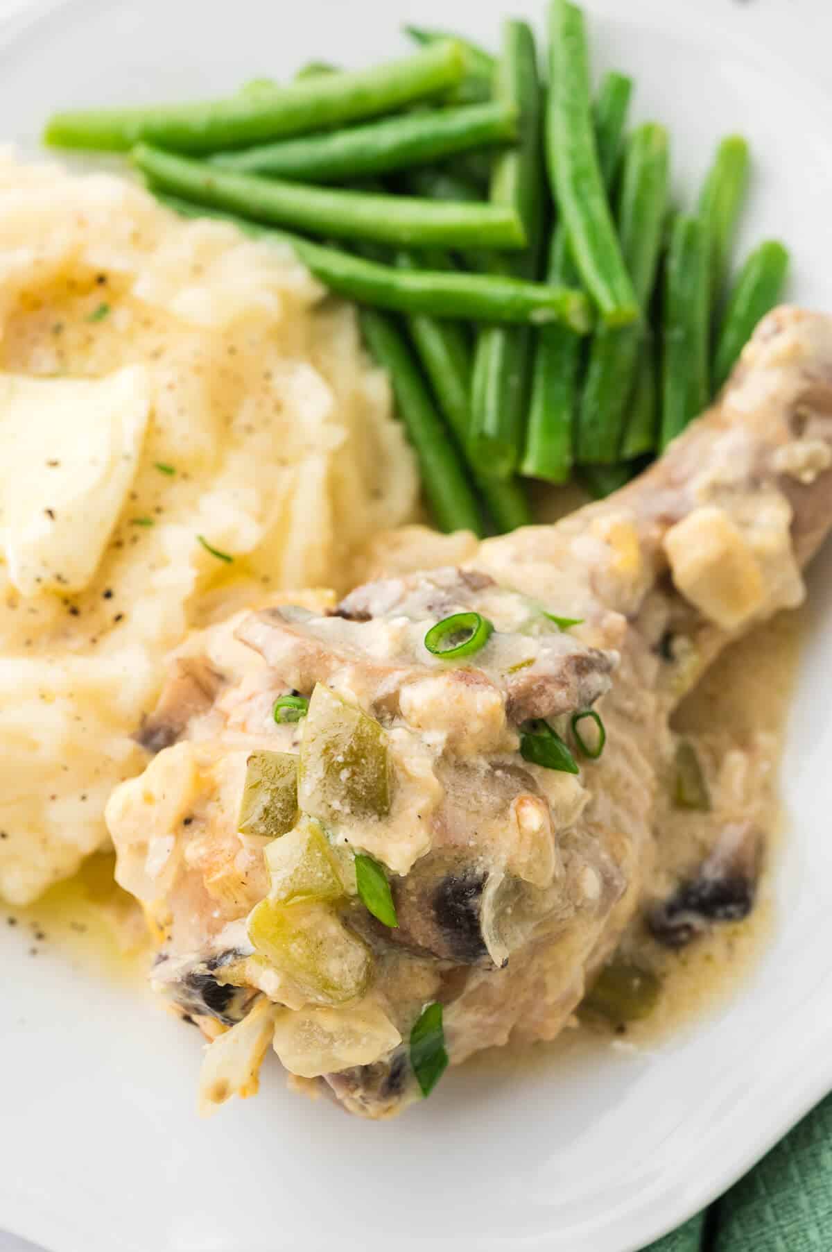 Smothered chicken on a plate with mashed potatoes and green beans.