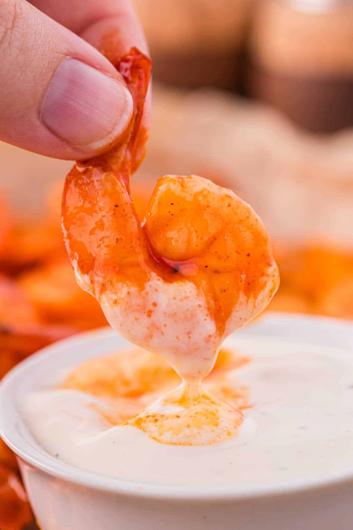 A hand holding a buffalo shrimp dipping in ranch dipping sauce.