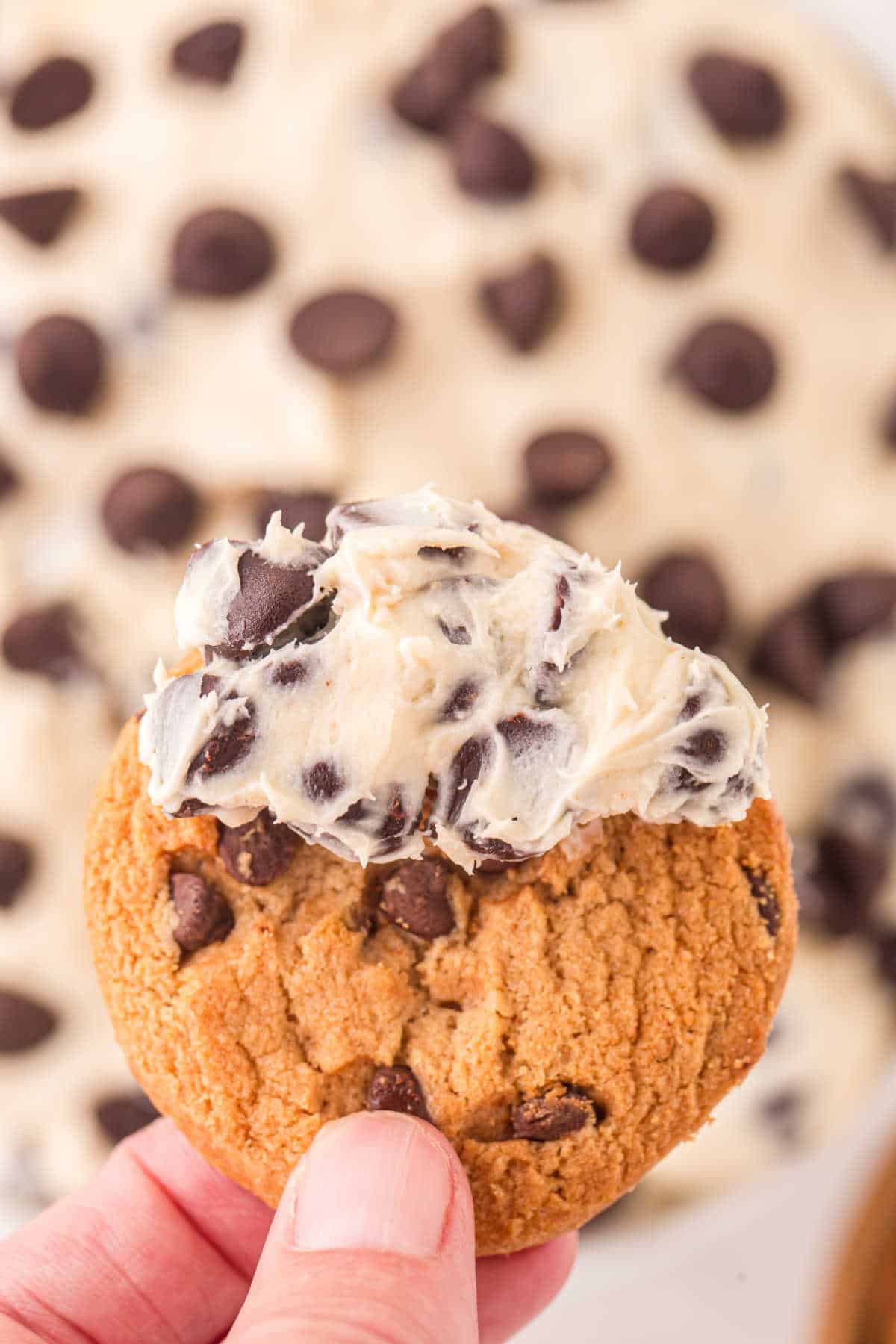 A chocolate chip cookie with cookie dough dip on it.