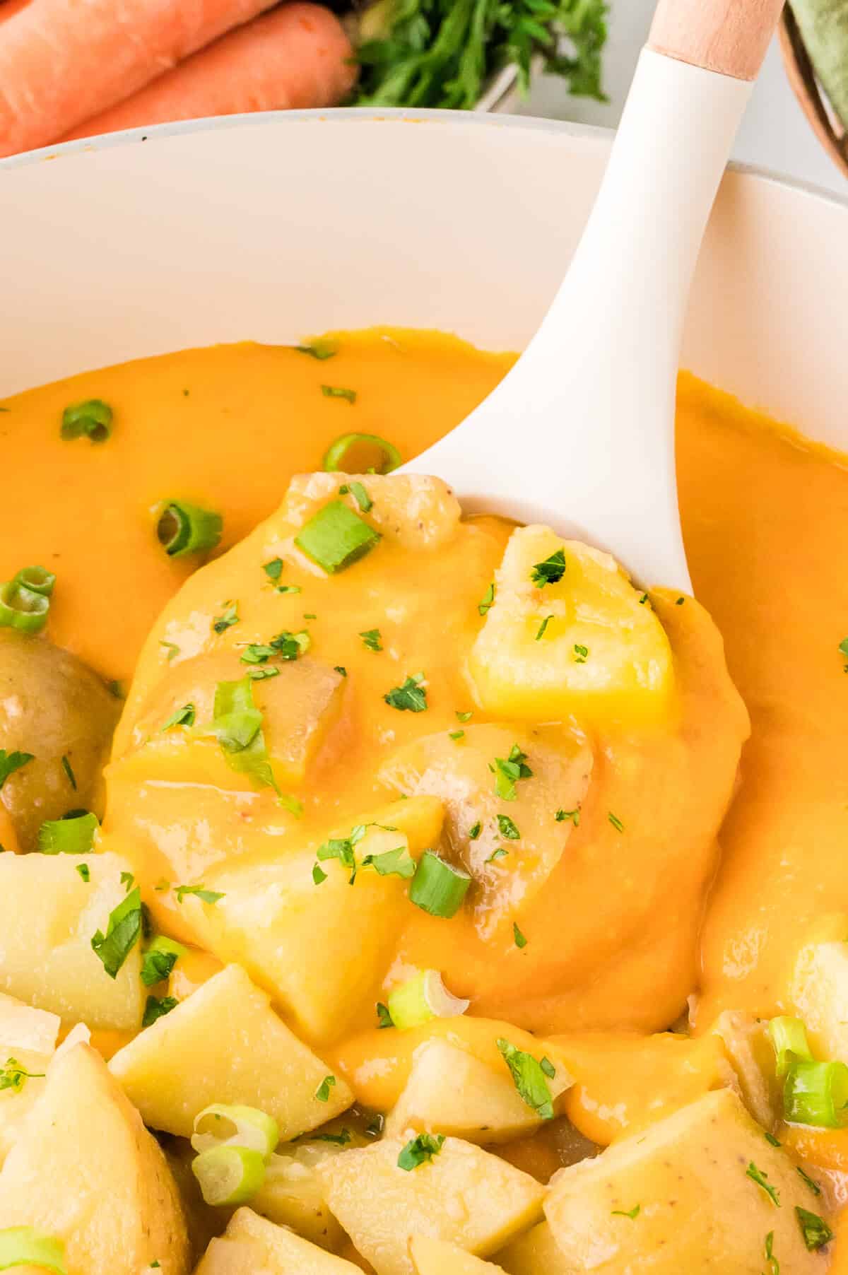 A white ladle with carrot and potato soup.