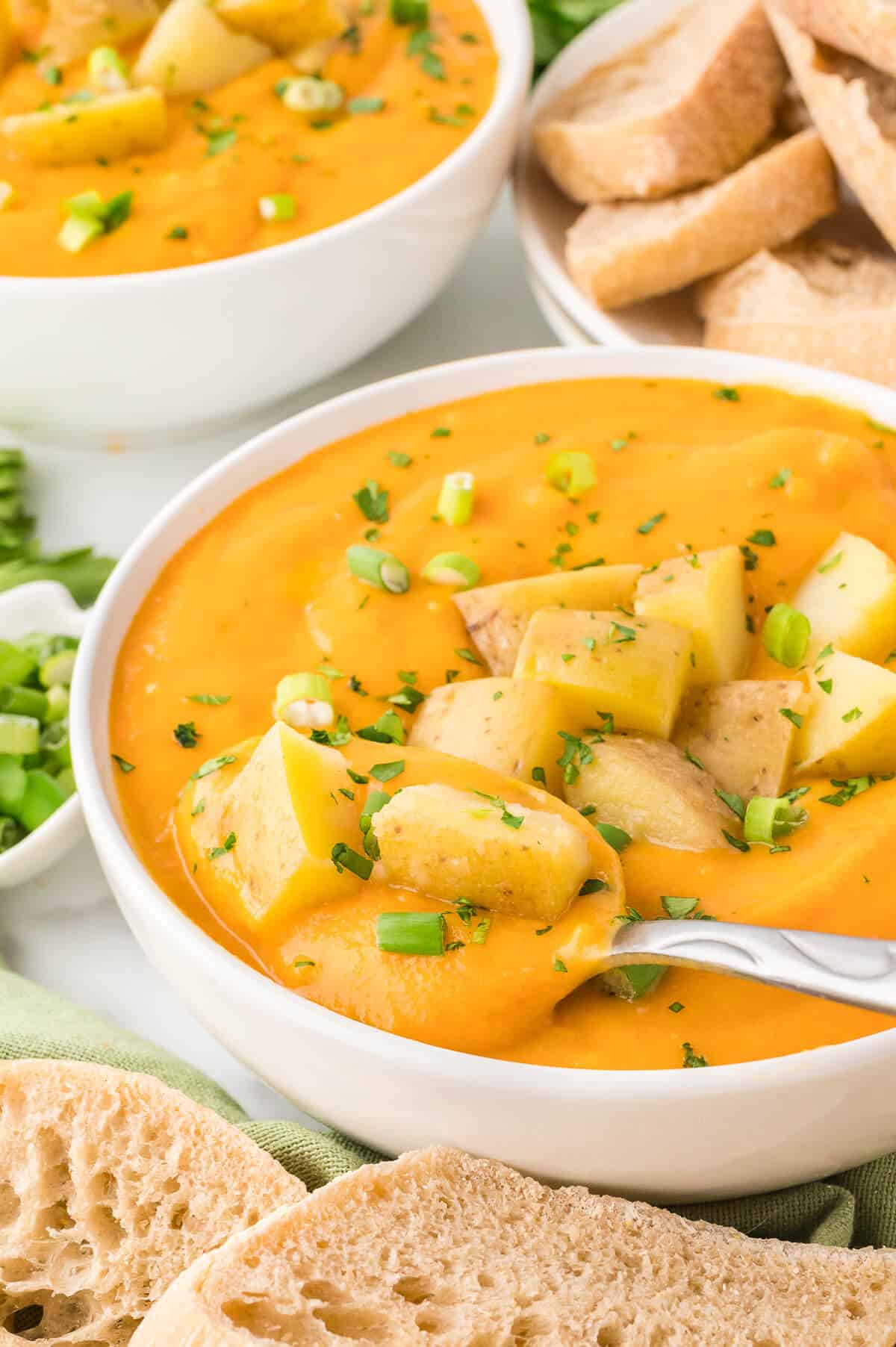 A bowl of carrot and potato soup with a spoon.