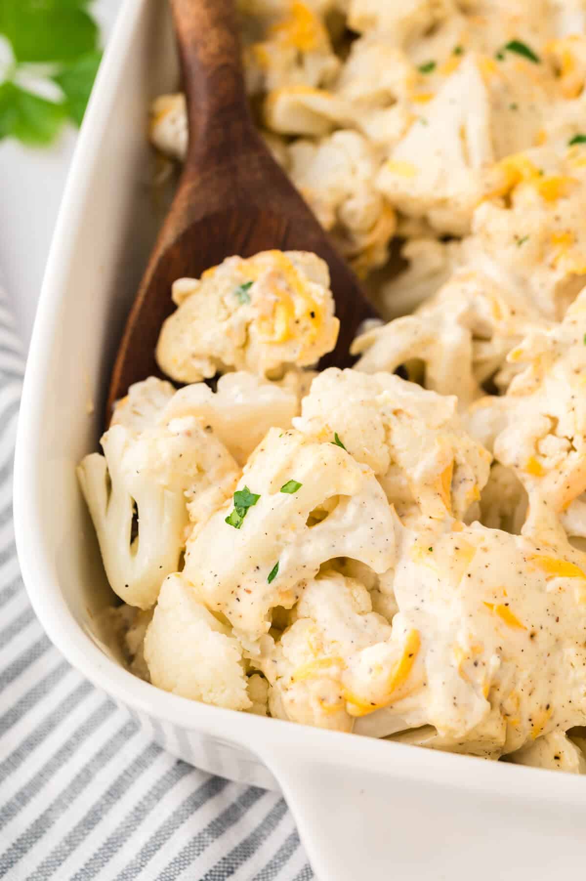 Creamy cauliflower in a baking dish with a wooden spoon.