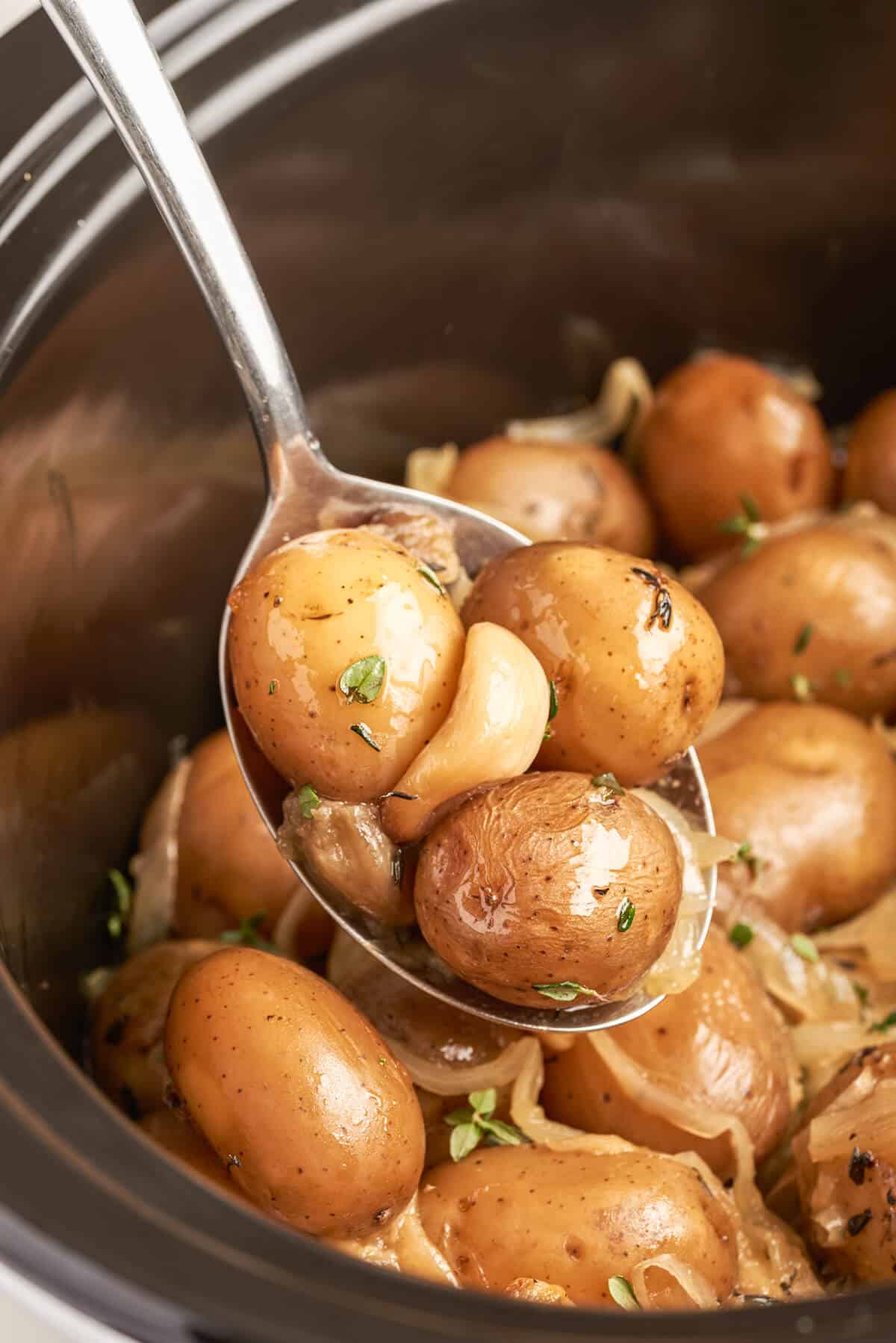 A serving spoon in a slow cooker with garlic potatoes.