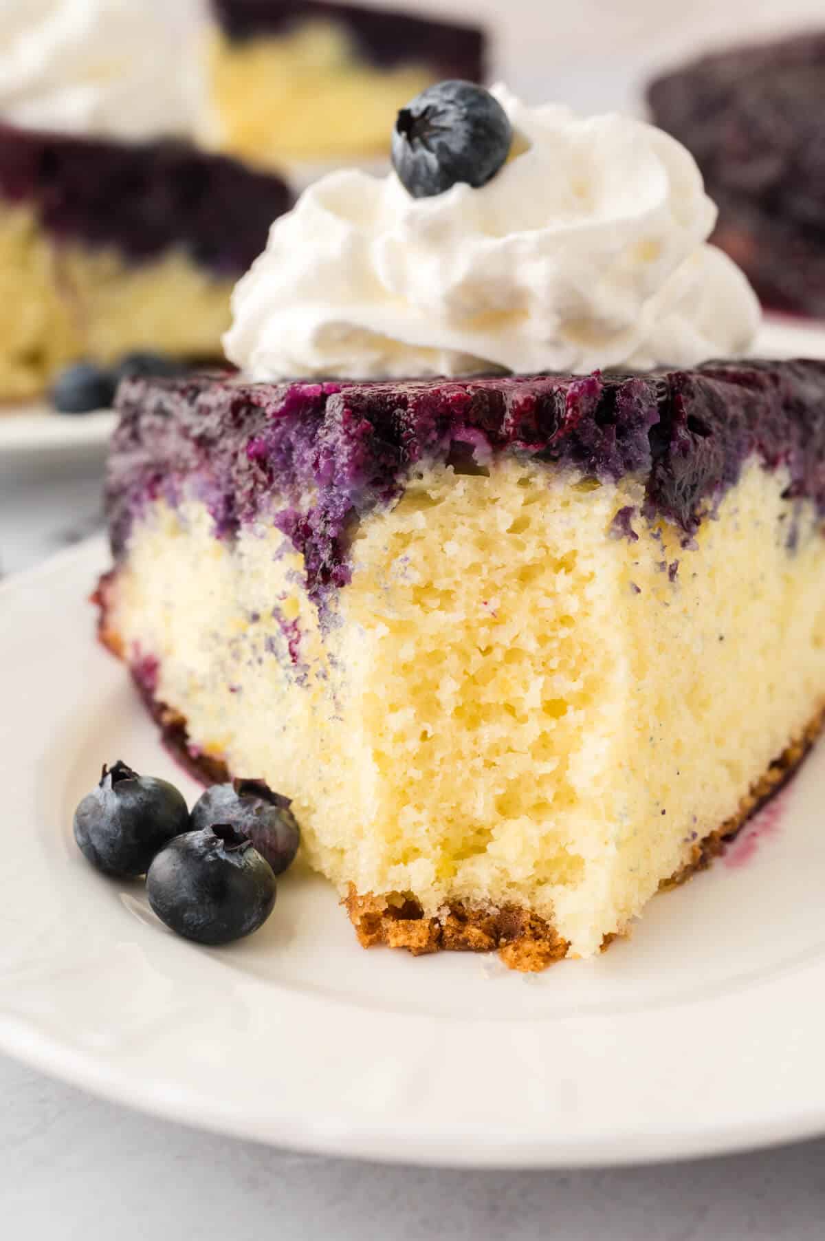 A slice of blueberry upside down cake on a plate with a bite off the end.