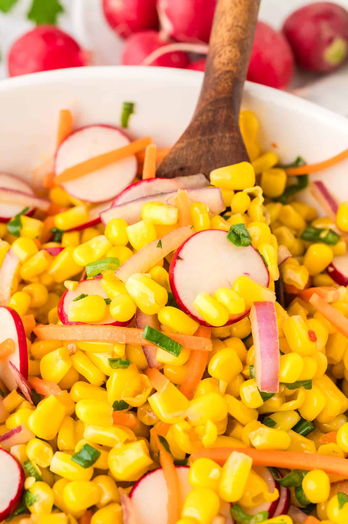 Corn Salad in a bowl with a wooden spoon.