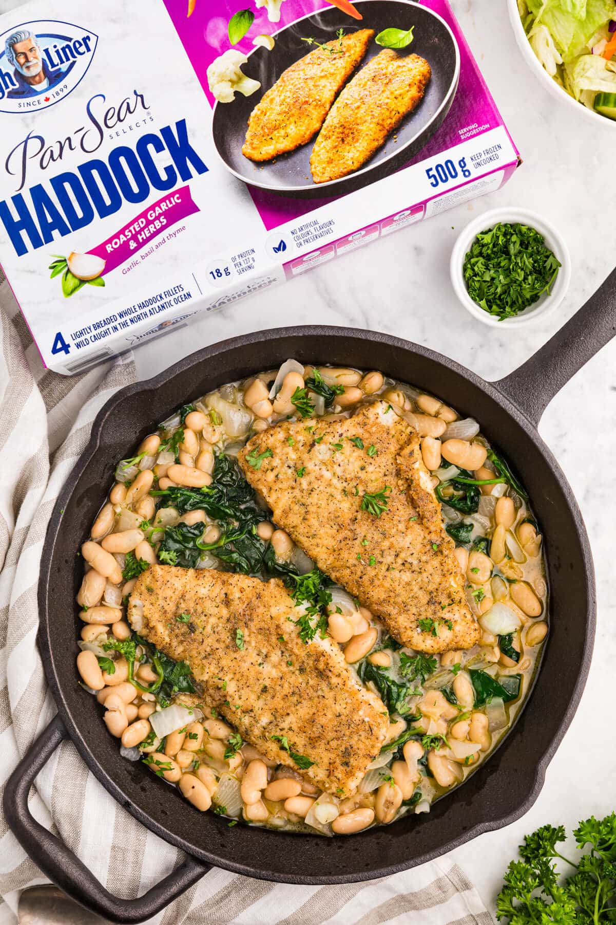 Haddock with spinach and white bean ragout in a cast iron pan.