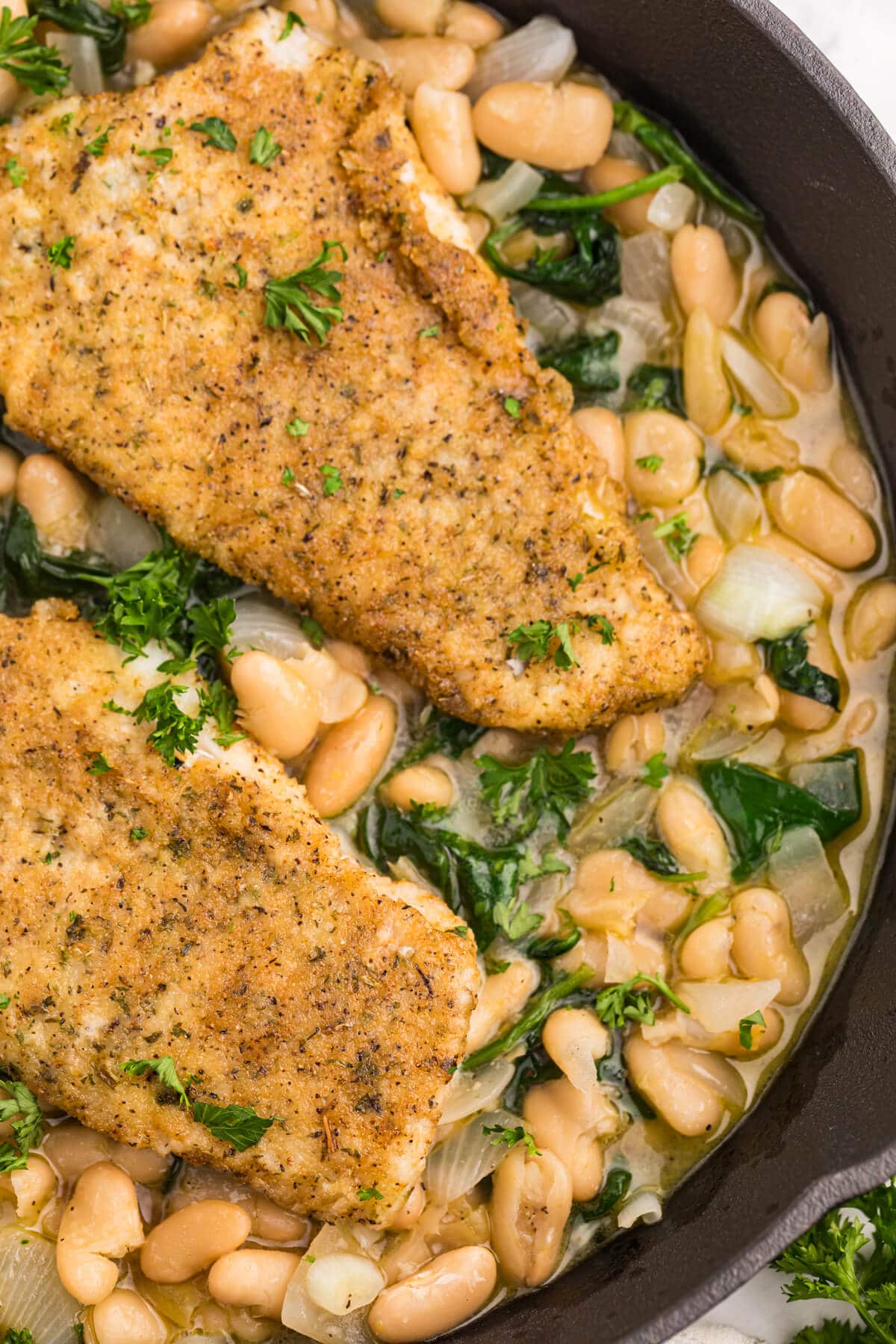 Haddock with spinach and white bean ragout in a cast iron pan.