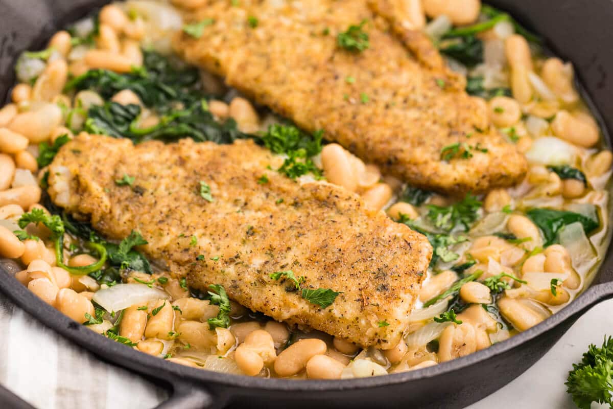 Haddock with spinach and white bean ragout in a cast iron pan.