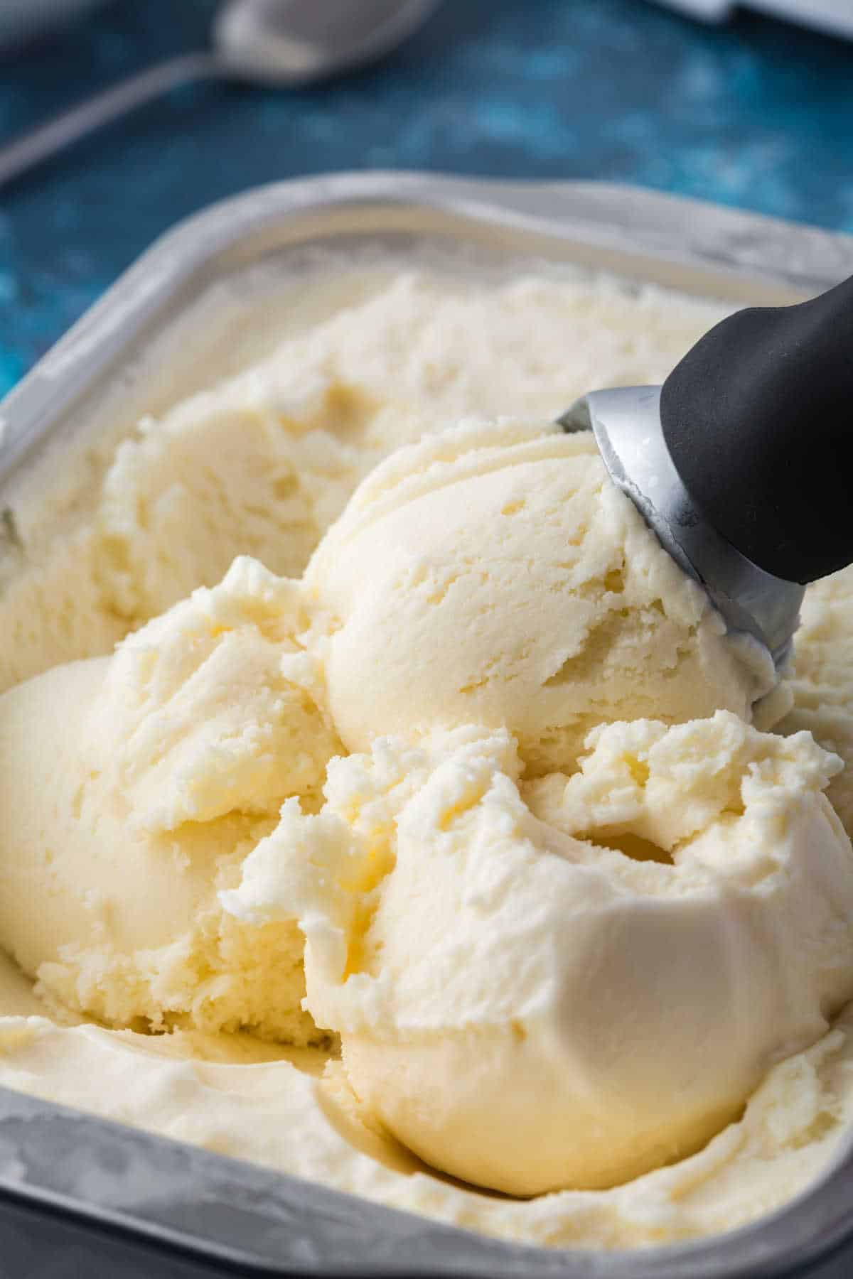 Homemade vanilla ice cream in a tub with an ice cream scoop.