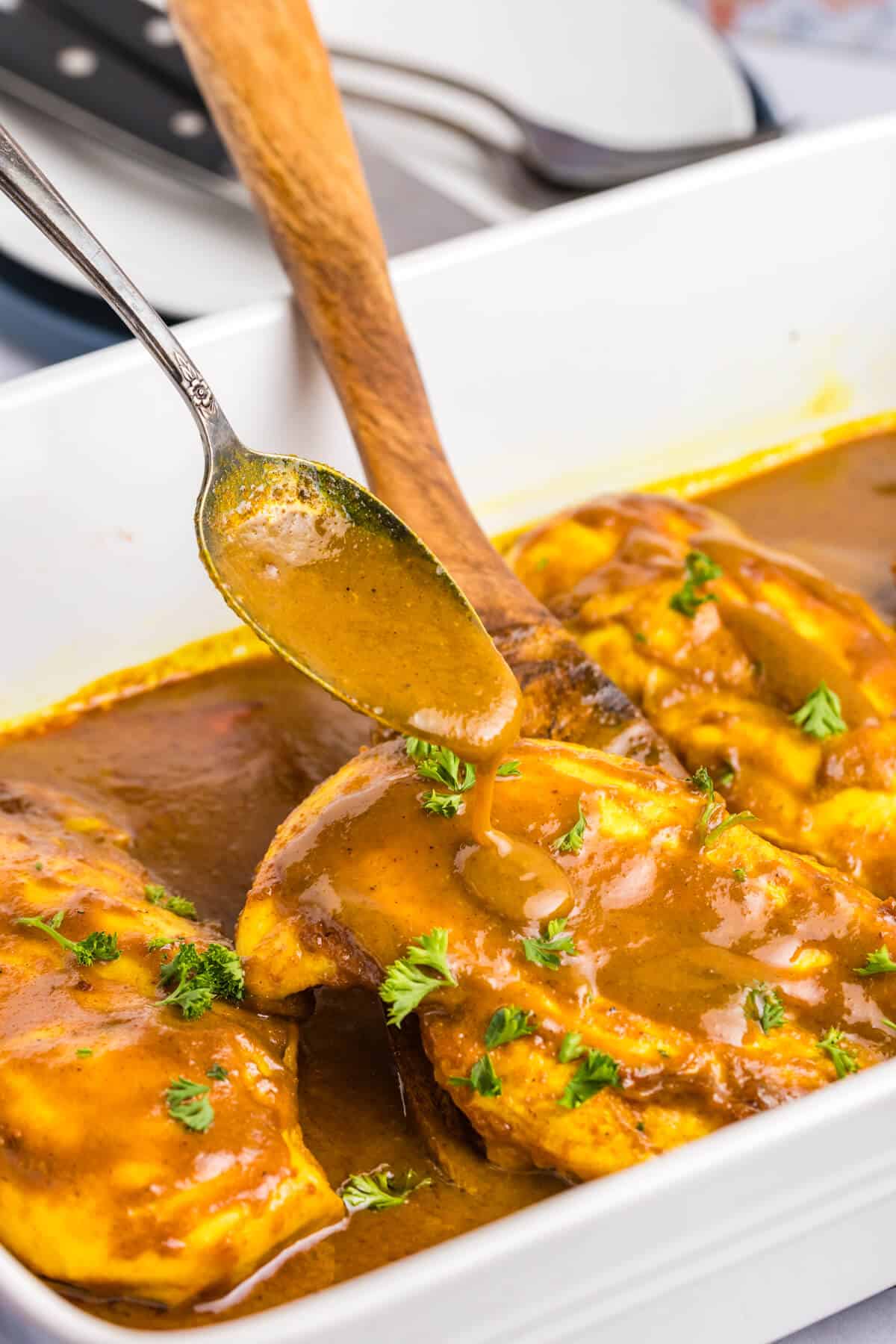 Honey curried chicken in a pan with a spoon pouring on sauce.