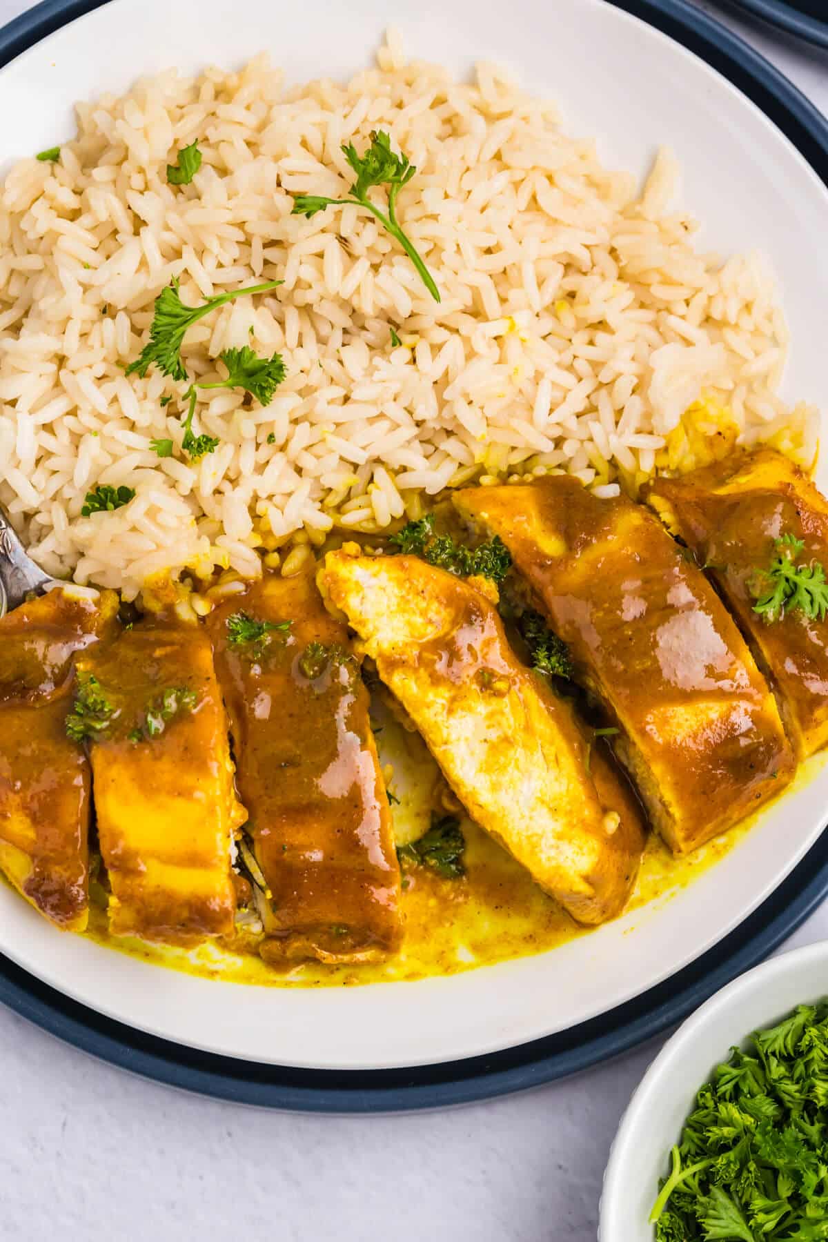 Honey curried chicken on a plate cut into pieces with white rice.