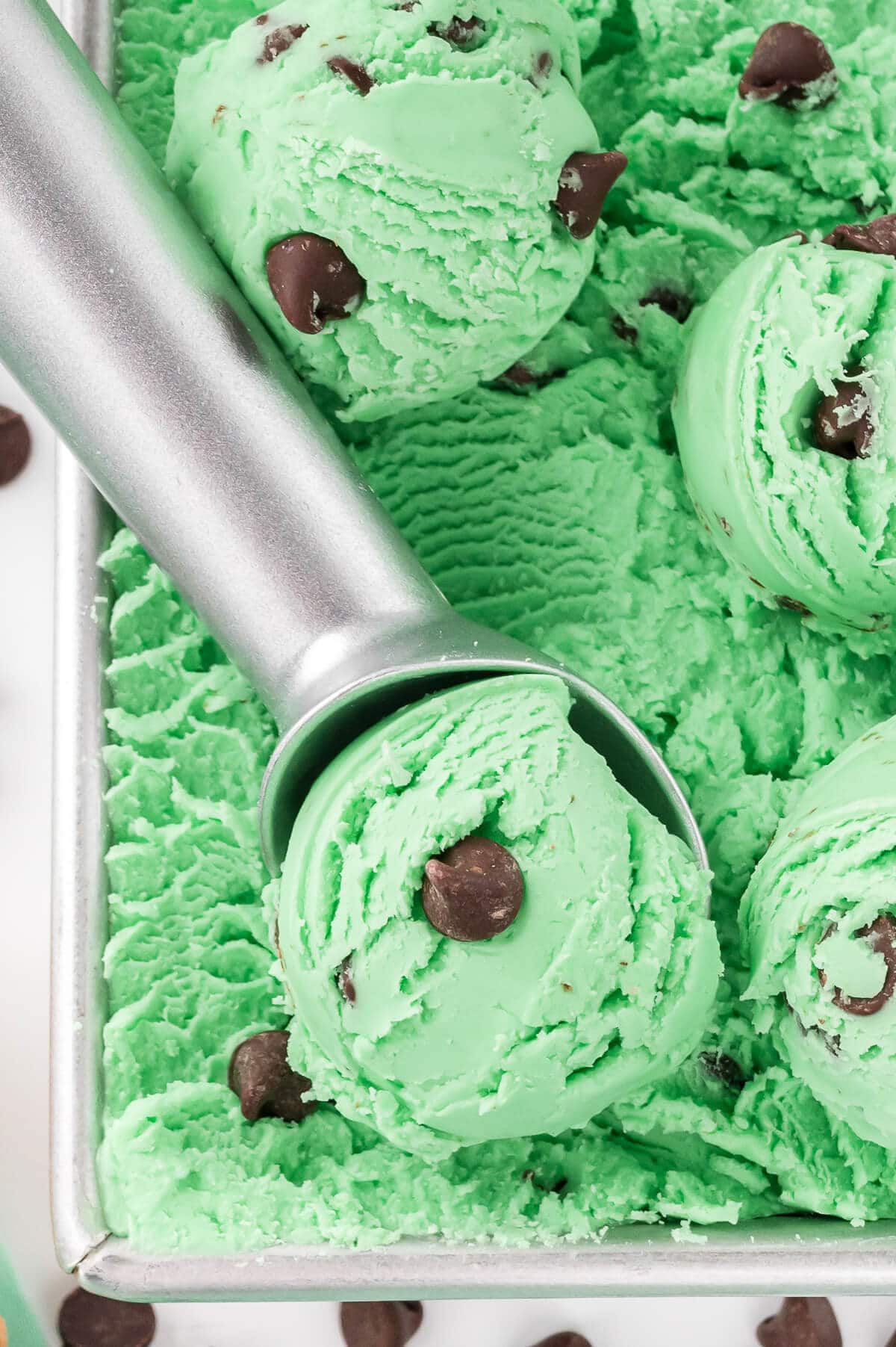 Mint chocolate chip ice cream in a container with an ice cream scoop.