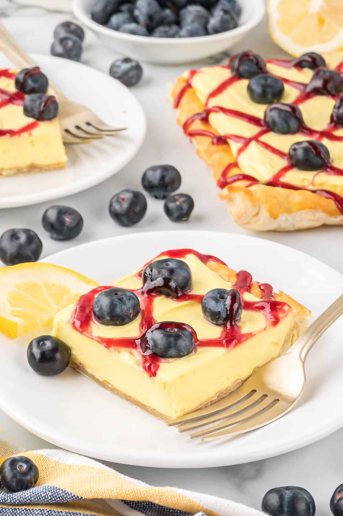 A slice of blueberry lemon tart on a plate with a fork.